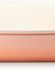 A rectangular ceramic baking dish with a warm peach-pink exterior and a glossy off-white interior, featuring side handles on a white background.