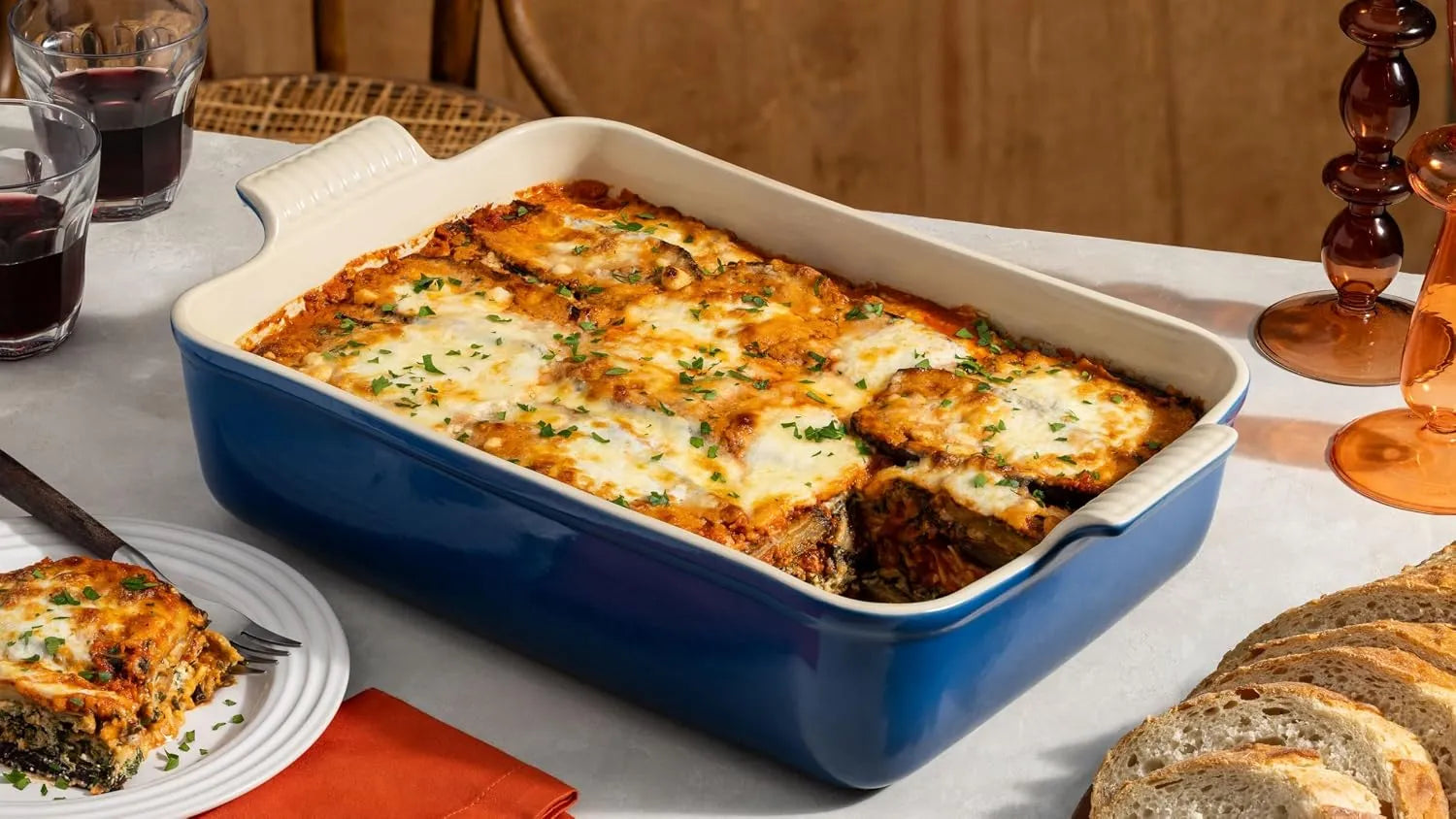 Baked dish in a blue casserole dish on a table with bread and glasses.