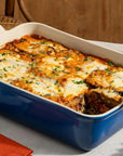 Baked dish in a blue casserole dish on a table with bread and glasses.