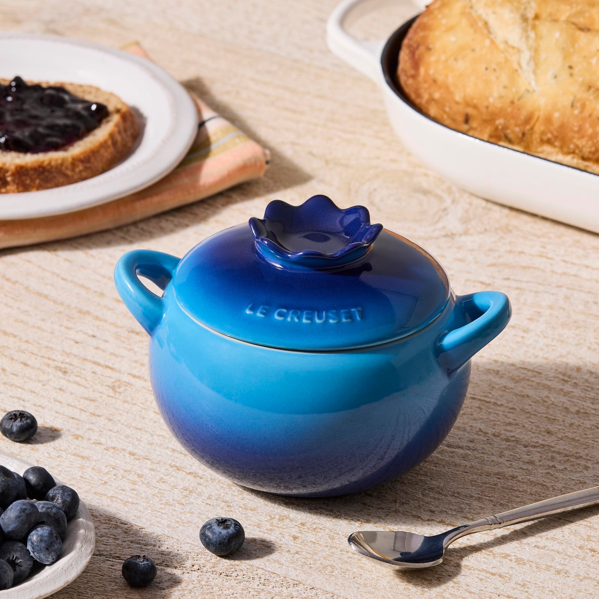 Blue Le Creuset pot on a table with bread and berries