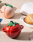 Colorful ceramic pots shaped like strawberries, peaches, and blueberries on a wooden table with bread and berries.