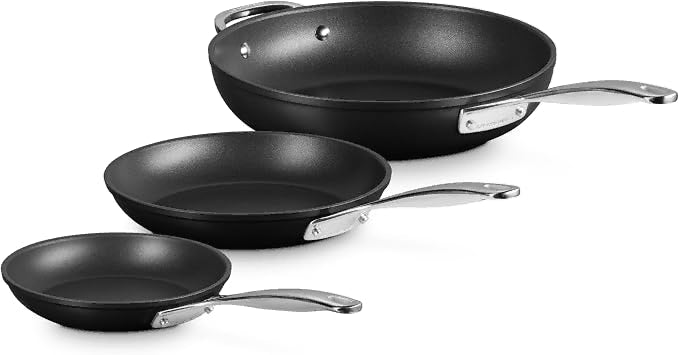 Three black nonstick frying pans in different sizes with silver metal handles, arranged diagonally on a white background.