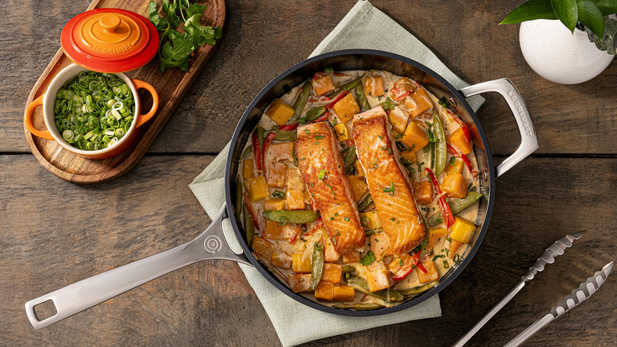 Skillet with salmon and vegetables on a wooden table