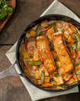 Skillet with salmon and vegetables on a wooden table