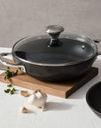 Black frying pan with a lid on a wooden cutting board against a gray background