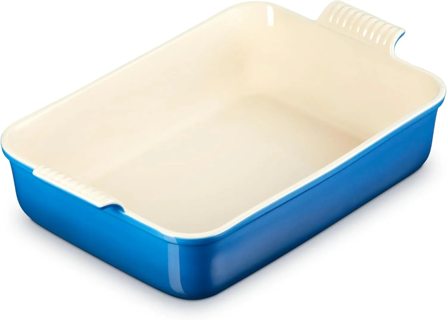 A rectangular ceramic baking dish with a vibrant blue exterior and a cream-colored interior, featuring a ridged handle on the top right.