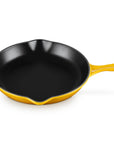 A yellow enameled cast iron skillet with a black non-stick interior, featuring a single loop handle on the left and a long straight handle on the right, shown on a white background.