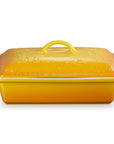 A yellow rectangular casserole dish with a matching lid, featuring white side handles and a floral embossed pattern on the lid, set against a plain white background.