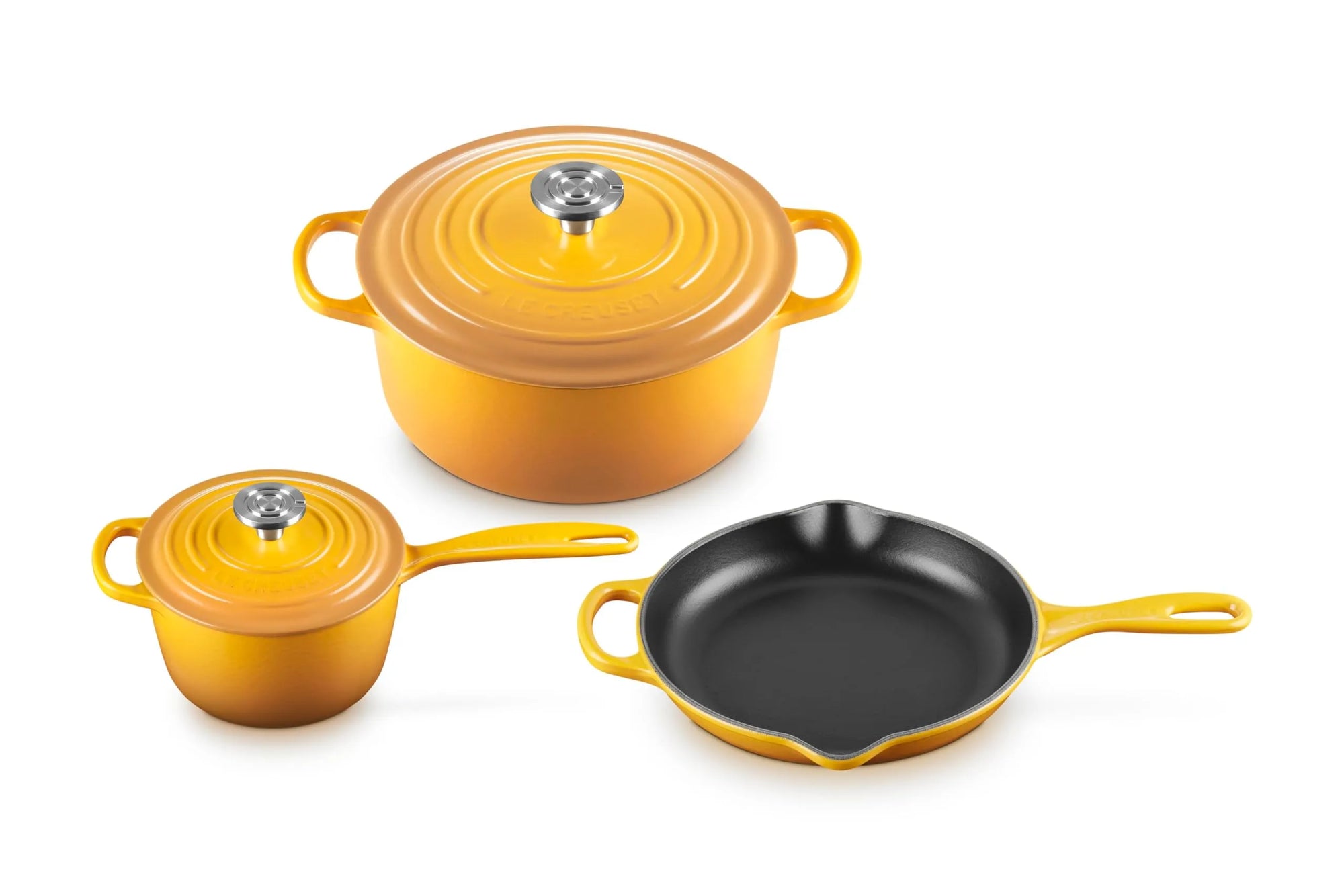 A three-piece cookware set in a bright yellow-orange enamel finish, including a lidded pot, a smaller lidded pot, and a skillet with a black interior, shown on a white background.