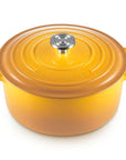 A yellow-orange enameled cast iron Dutch oven with a matching lid and side handles, featuring a silver metal knob, shown on a white background.