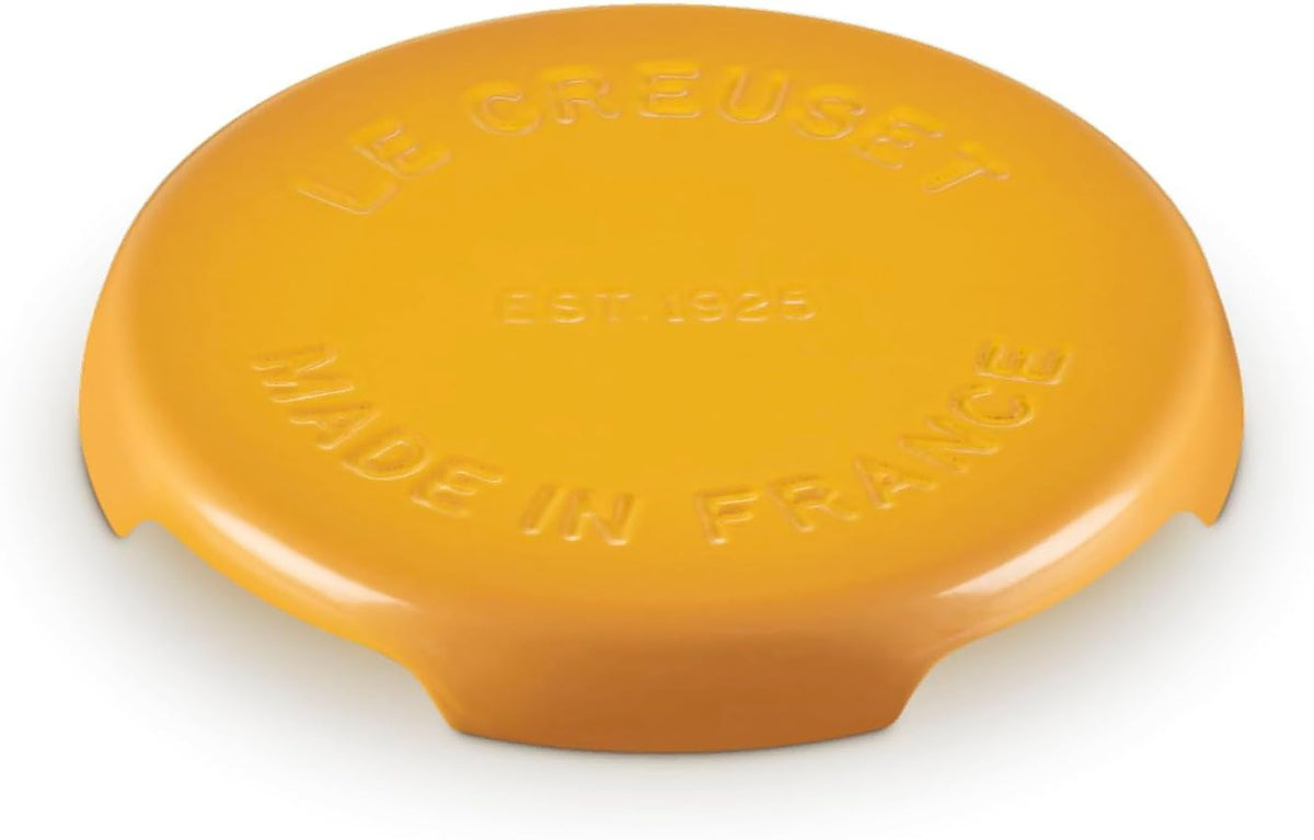 A yellow Le Creuset round trivet with embossed text reading 'LE CREUSET', 'EST. 1925', and 'MADE IN FRANCE' on a white background.