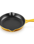 A yellow enameled cast iron skillet with a black non-stick interior, featuring a single loop handle and a small side handle, shown on a solid white background.