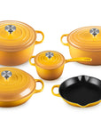 A 5-piece enameled cast iron cookware set in a vibrant yellow-orange color, including three pots of varying sizes with lids, a small saucepan with lid, and a black skillet, arranged on a clean white background.