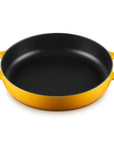 A round cast iron skillet with a yellow exterior and a black non-stick interior, featuring two loop handles on a white background.