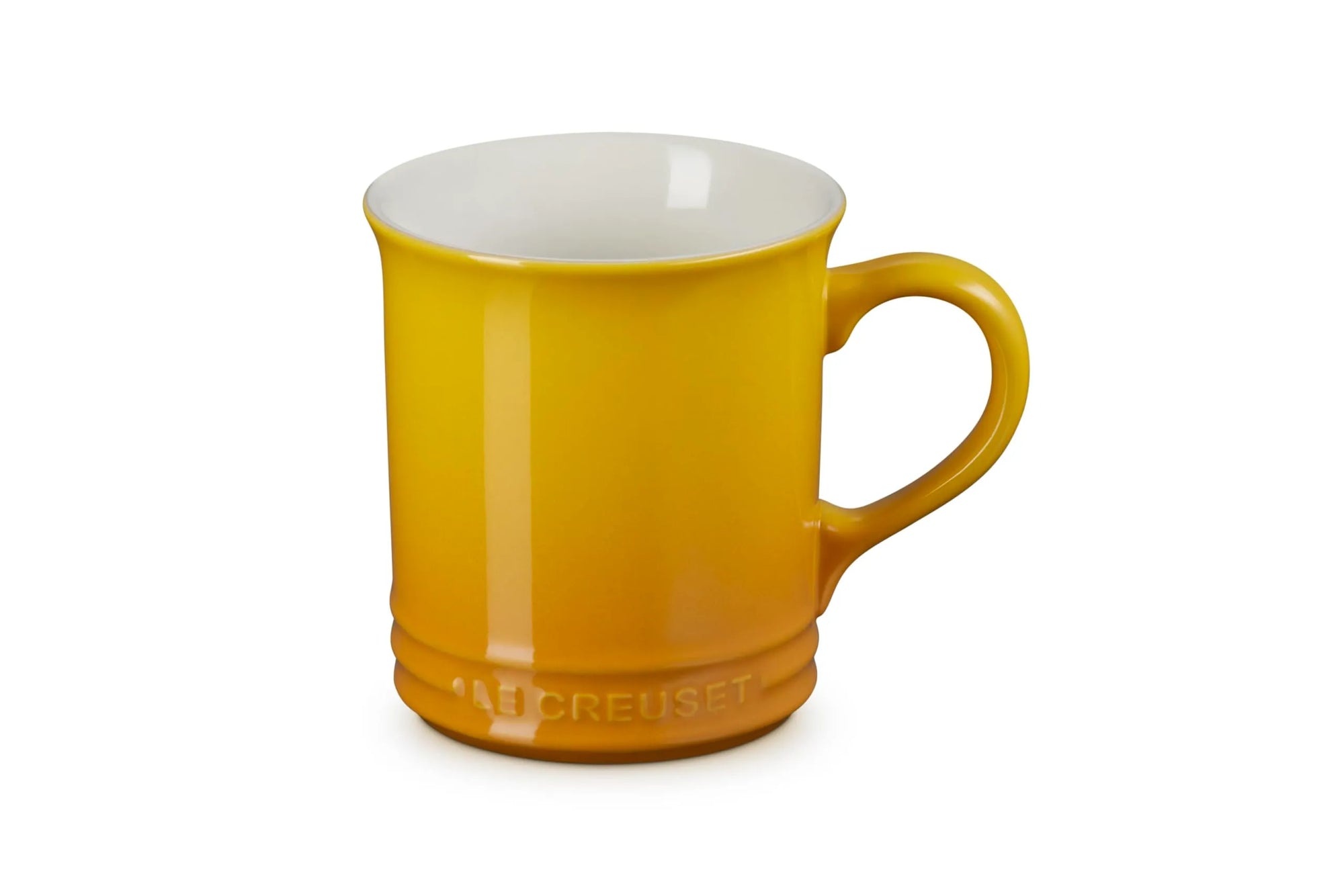 A Le Creuset ceramic mug in a vibrant mustard yellow color, featuring a glossy finish, a curved handle, and the embossed Le Creuset brand name at the base, set against a plain white background.