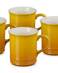 Four Le Creuset ceramic mugs in a warm mustard yellow color with a glossy finish and white interiors, arranged on a clean white background.