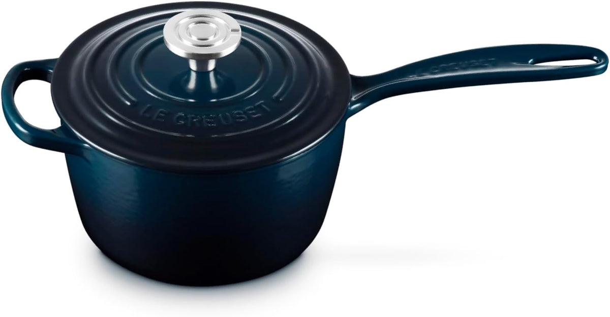 A Le Creuset dark blue enameled cast iron saucepan with a matching lid and a silver knob, shown on a white background.