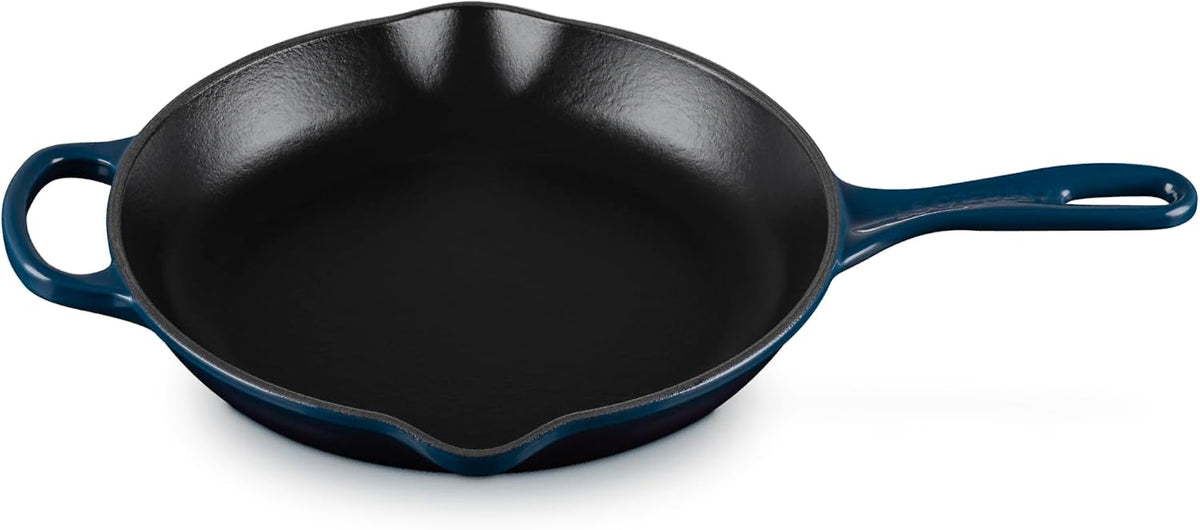 A dark blue enameled cast iron skillet with a black non-stick interior, featuring a single loop handle on the left and a long straight handle on the right, shown on a white background.