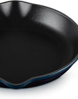 A dark blue enameled cast iron skillet with a black non-stick interior, featuring a single loop handle on the left and a long straight handle on the right, shown on a white background.