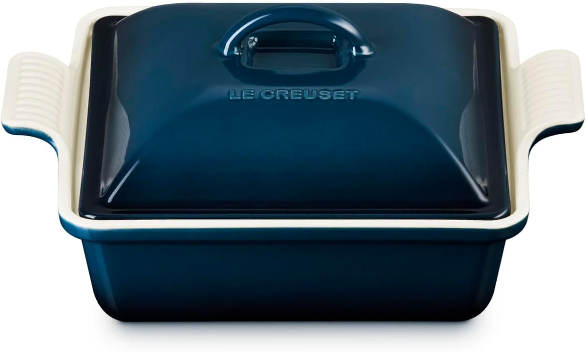 A Le Creuset lidded casserole dish in dark blue with cream-colored handles, shown on a clean white background.