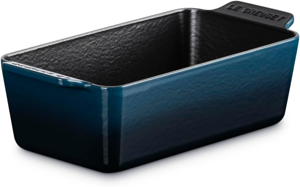A Le Creuset rectangular loaf pan in a deep teal blue color, featuring a textured dark interior and a matching handle with the brand name embossed.