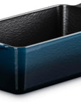 A Le Creuset rectangular loaf pan in a deep teal blue color, featuring a textured dark interior and a matching handle with the brand name embossed.
