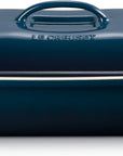A Le Creuset rectangular casserole dish with a matching lid, featuring a deep navy blue enamel finish and contrasting white side handles.