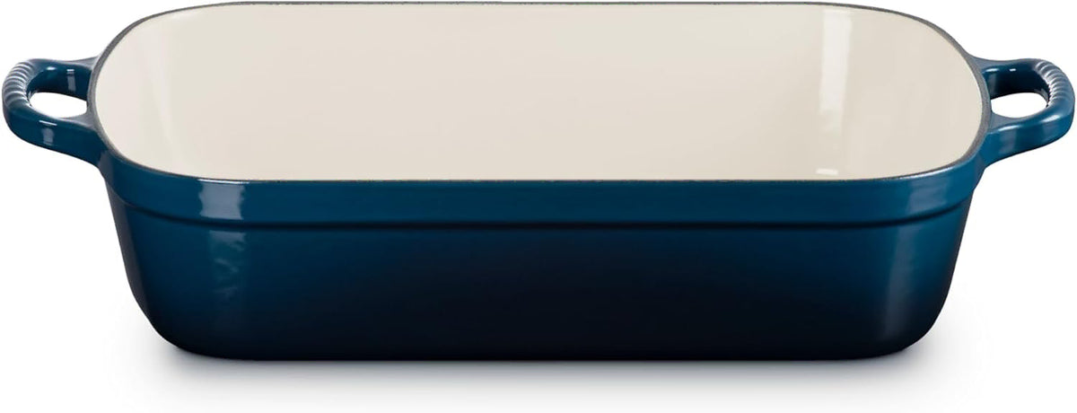 A rectangular baking dish with a deep blue exterior and a cream-colored interior, featuring two side handles.