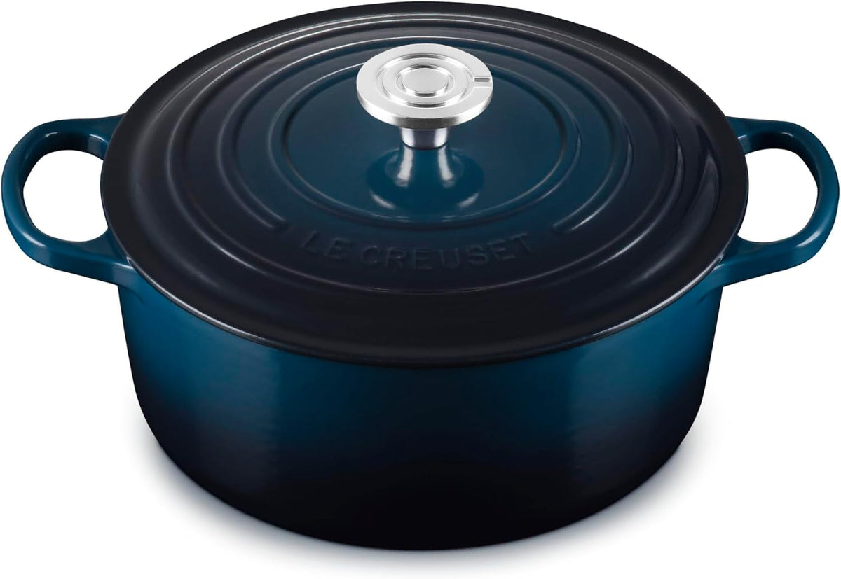 A Le Creuset round enameled cast iron Dutch oven with a lid, featuring a deep navy blue color and a silver stainless steel knob, set against a plain white background.