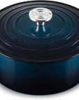 A Le Creuset round enameled cast iron Dutch oven with a lid, featuring a deep navy blue color and a silver stainless steel knob, set against a plain white background.