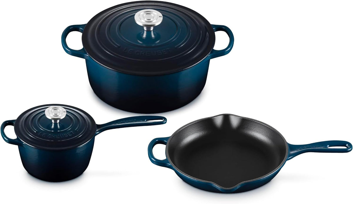 Three-piece Le Creuset cookware set in deep teal enamel, including a round lidded pot, a smaller lidded pot, and a skillet, shown on a white background.