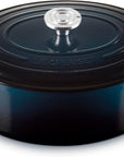 A Le Creuset round enameled cast iron Dutch oven with lid, in a dark blue color, featuring side handles and a silver knob, set against a plain white background.