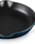 A cast iron skillet with a dark blue enameled exterior and a black non-stick interior, shown on a white background.