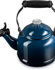 A dark blue enamel stovetop kettle with a black handle and spout, featuring a silver metal lid knob with the Le Creuset brand name.