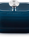 A Le Creuset oval lidded casserole dish in dark teal blue with a silver knob and side handles, shown on a white background.