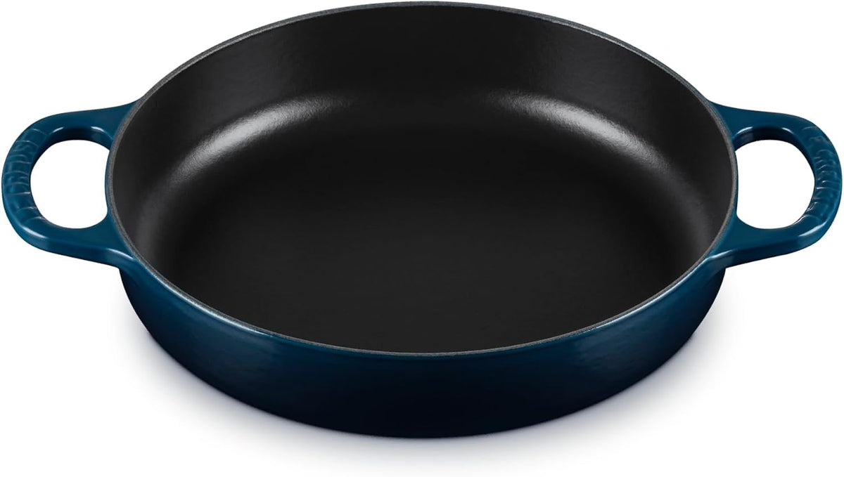 A round cast iron skillet with a dark blue exterior and a black non-stick interior, featuring two loop handles on a white background.