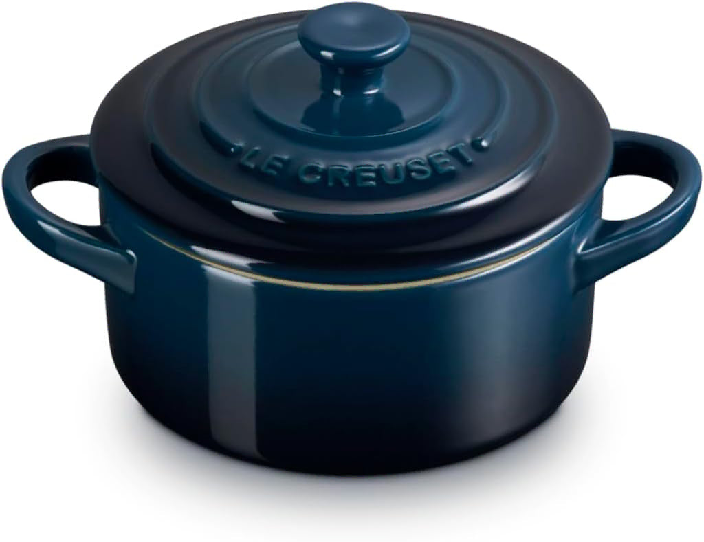 A dark blue Le Creuset enameled cast iron pot with a matching lid, featuring side handles and a gold accent line, shown on a white background.