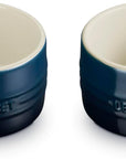 Two Le Creuset ramekins shown side by side on a white background, featuring a dark navy blue exterior with a cream-colored interior.