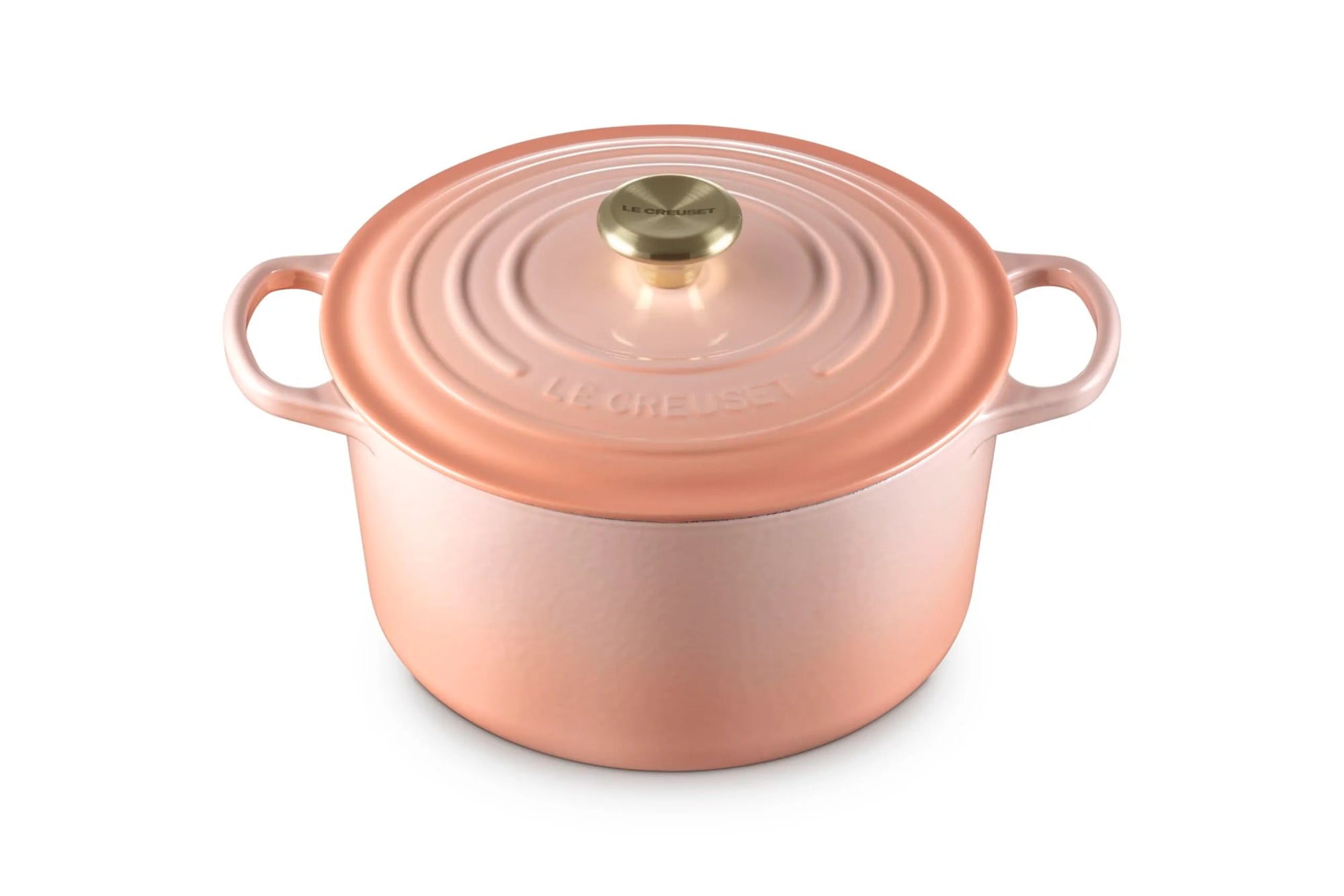 A Le Creuset round enameled cast iron pot with lid in a coppery rose gold finish, featuring two side handles and a gold-toned knob, set against a plain white background.