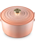 A Le Creuset round enameled cast iron pot with lid in a coppery rose gold finish, featuring two side handles and a gold-toned knob, set against a plain white background.