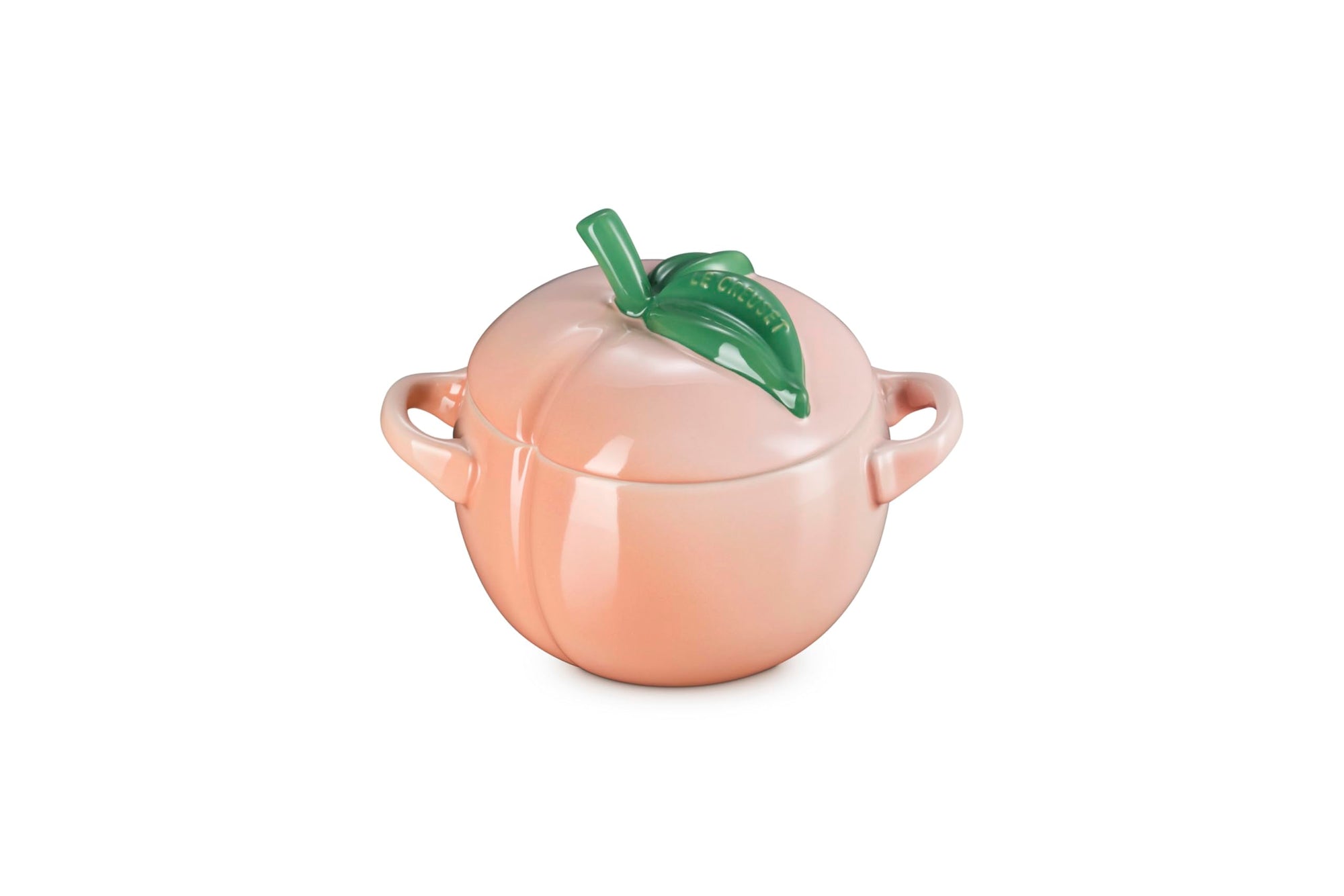 Peach-shaped ceramic container with a green leaf on a white background