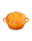 A persimmon cast iron pumpkin-shaped lidded cocotte dish with side handles, shown on a solid white background.
