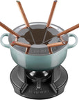Le Creuset fondue set with a light blue enameled pot, black cast-iron base, and copper-colored cheese forks and utensils, shown on a white background.