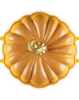 A Le Creuset pumpkin-shaped enameled cast iron Dutch oven lid, featuring a golden yellow-orange finish with a central gold logo and side handles, shown on a solid white background.