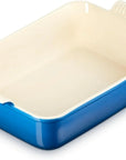 A rectangular ceramic baking dish with a vibrant blue exterior and a cream-colored interior, featuring a ridged handle on the top right.