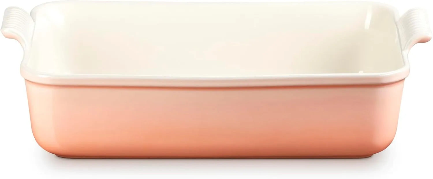 A rectangular ceramic baking dish with a warm peach-pink exterior and a glossy off-white interior, featuring side handles on a white background.