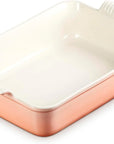 A rectangular ceramic baking dish with a peach exterior and a cream-colored interior, featuring integrated side handles with a ribbed texture.