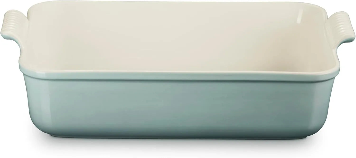 A rectangular ceramic baking dish with side handles, featuring a pale mint green exterior and a warm cream-colored interior, shown against a plain white background.