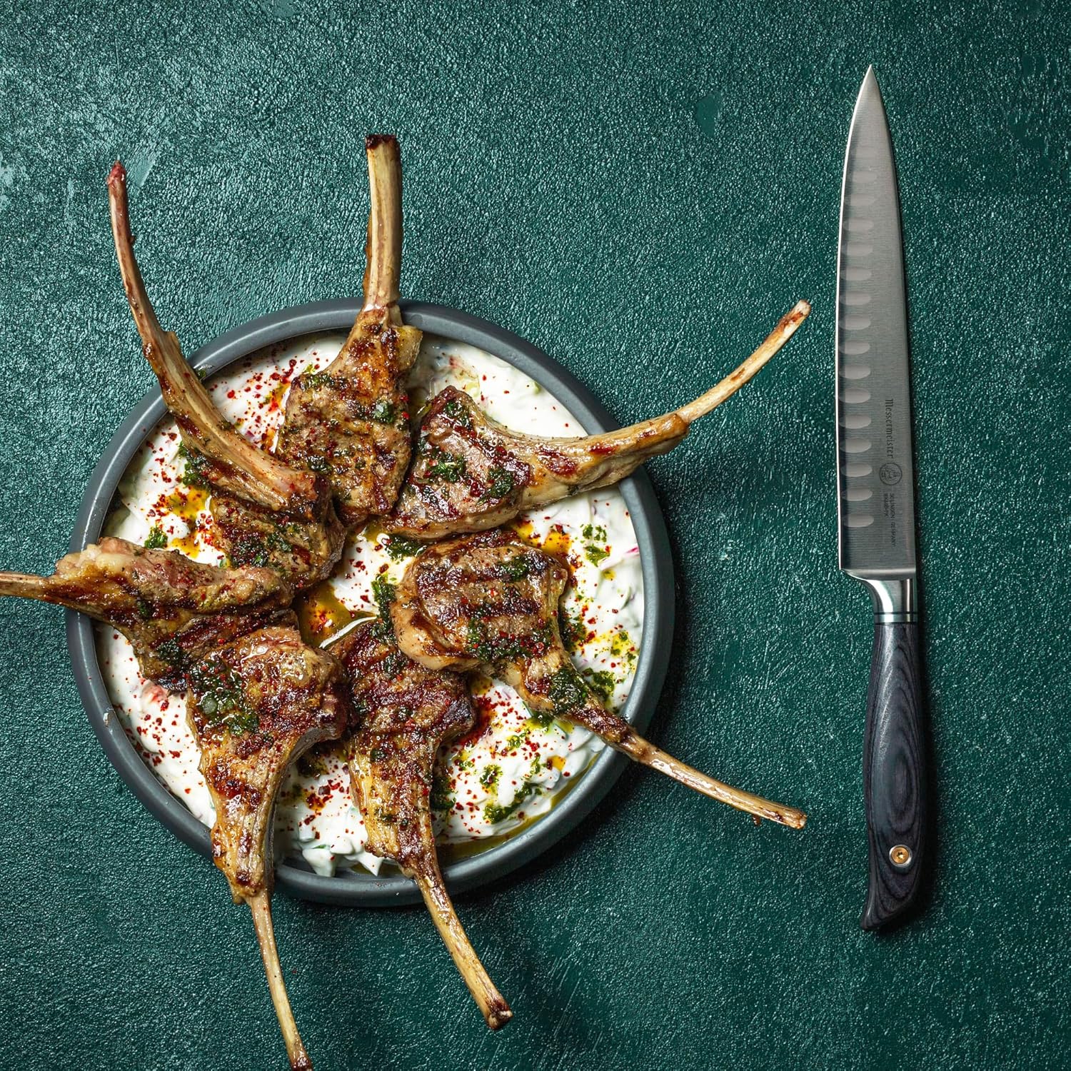 Grilled lamb chops on a plate with a knife on a green background