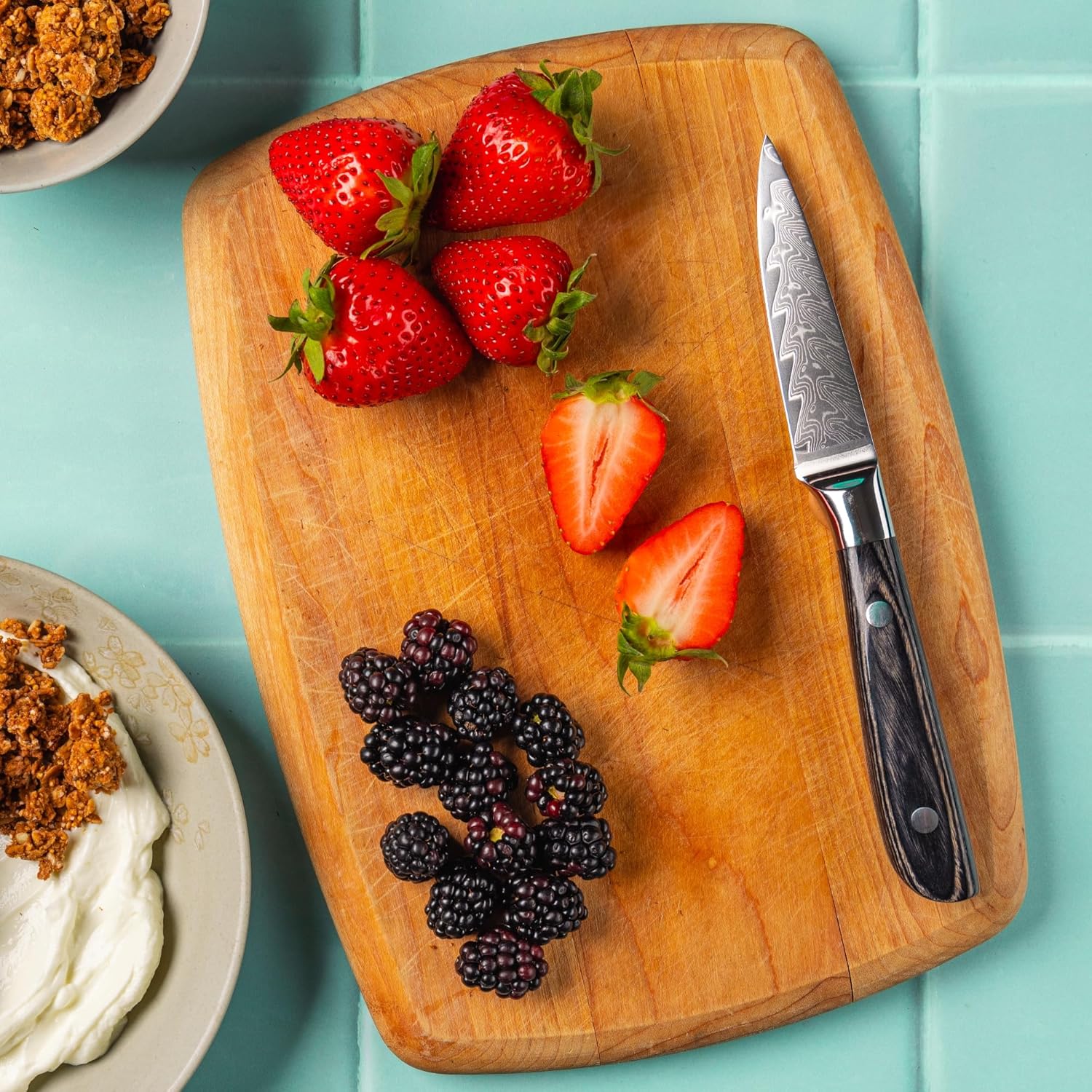 Wooden cutting board with strawberries, blackberries, and a knife on a turquoise background